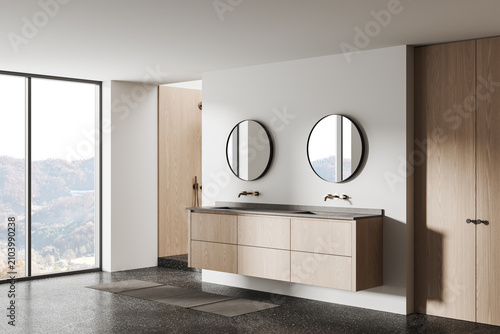 Minimalist bathroom interior featuring floating wooden vanity, dual circular mirrors, terrazzo floor and large window overlooking serene landscape. 3D Rendering