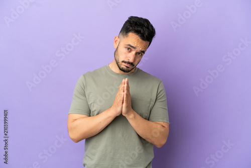 Young caucasian man isolated on purple background keeps palm together. Person asks for something