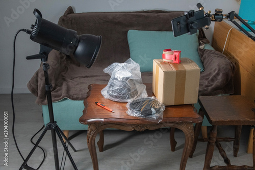 Creating a home studio setup for unboxing products, featuring a professional light, smartphone recording on a stand, and a package with bubble wrap on a table