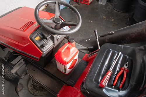 Riding lawn tractor showing a bottle of engine oil and various hand tools, ready for outdoor equipment maintenance and gardening work in a garage setting