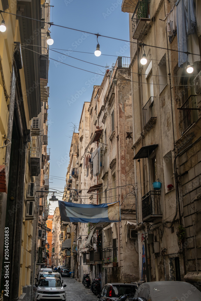 Fototapeta premium Naples, italy. December 29, 2024. Buildings lining a narrow street in the historic center of naples, italy, with laundry drying on balconies and string lights overhead