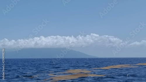 Cuadro en lienzo Distant land appears beyond the calm blue ocean beneath a line of clouds