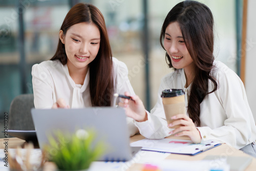Asian businesswomen collaborating and discussing project ideas during an informal meeting in a modern office, using a laptop and sharing insights for successful teamwork