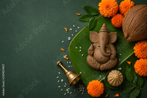 Eco Friendly Clay Ganesha Figurine on Banana Leaf with Marigolds, Coconut, Modak, Rice, Green Leaves, and Brass Bell Arranged on a Dark Green Festival Background