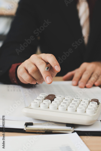 Accountant reviewing printed financial reports at messy office desk with calculator and sticky notes under soft window daylight for audit and corporate finance work