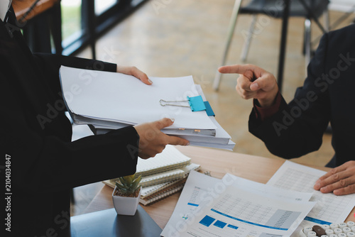 Accountant reviewing printed financial reports at messy office desk with calculator and sticky notes under soft window daylight for audit and corporate finance work