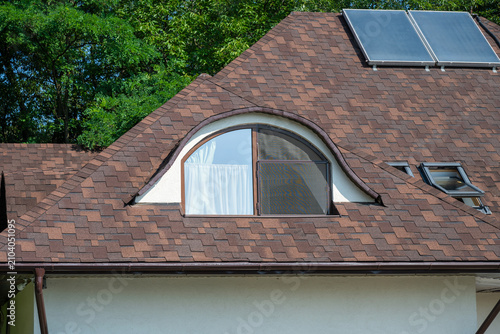 Cuadro en lienzo a detailed exterior view of a residential home's brown asphalt shingle roof, highlighting a prominent arched dormer window, modern skylights, and solar panels