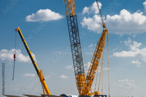 Tableau sur toile the towering yellow lattice and telescopic booms of heavy construction cranes reaching into a bright blue sky dotted with fluffy cumulus clouds