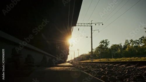 On sunlit railway track, freight train speeds past as its wheelsets glide over sleeper rails. The close-up view underscores railway infrastructure and routine track maintenance in open field settings