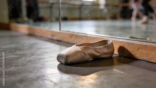 Fotografija A single, well-worn ballet shoe rests on the floor before a large rehearsal mirror