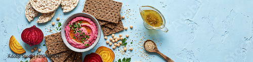 Healthy Vegan Snack Arrangement with Beet Hummus, Crisps, and Raw Ingredients. Top-Down Culinary Flat Lay Featuring Vibrant Beetroot Dip and Artisanal Crackers on plaster blue background.