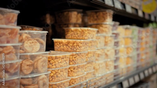 A young woman carefully examines a container of assorted nuts on a store shelf reading the label among rows of packaged nuts and dried goods