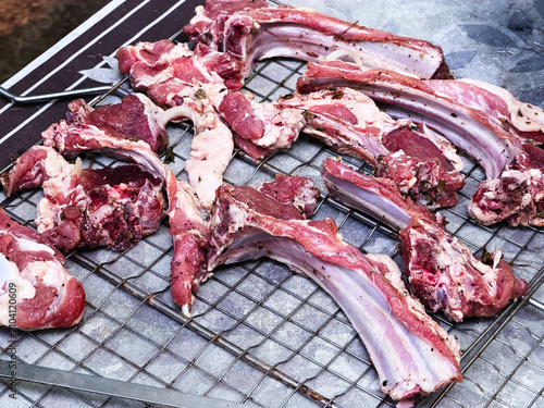 Raw lamb ribs and pieces of meat laid out on a metal grill before cooking. Fresh lamb with a natural texture is ideal for cooking shish kebab, barbecue, grill and traditional meat dishes. The photo