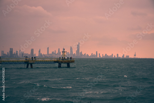Pink winter sunset with tall buildings of Kuwait city in Background and cold water of sea and in between fishing pier