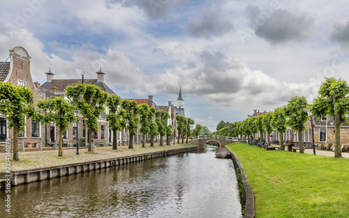Obraz na plátně Canal town view with historic houses, tree-lined quay and stone bridge in Sloten