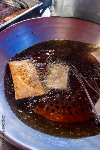 Close up of golden brown pastel fried dough being lifted from hot oil in a large pan at a street food market