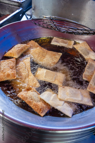 Close up of golden brown pastel fried dough being lifted from hot oil in a large pan at a street food market