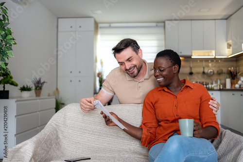 Couple sharing a moment on a couch in their living room while looking at papers