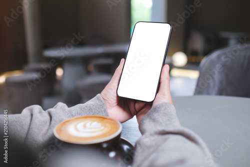 Mockup image of a woman holding mobile phone with blank desktop screen in cafe