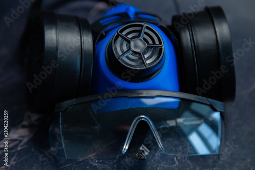 Close-up of a blue respirator with black filters and goggles on a dark marble background. Concept of industrial safety, respiratory and eye protection, reliable equipment for work. High quality photo