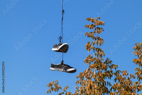 Old sneakers hanging on a wire against blue sky. Shoefiti concept with worn shoes dangling from telephone line