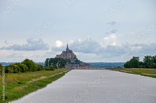 Photography Mont-Saint-Michel viewed from canal with bridge crossing, green fields and trees, landscape, UNESCO heritage site