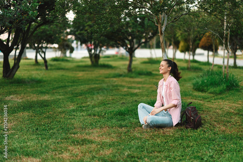 Obraz na płótnie A smiling woman sits on green grass in a sunlit park, enjoying a peaceful moment