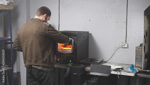 Фотография A blacksmith opens a glowing furnace, places a knife blade inside, and closes the furnace during the metal quenching process