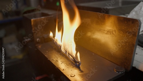 Canvas Print A blacksmith removes a red-hot knife blade from a furnace, immerses it in an oil bath, and it ignites in flames during the metal quenching process