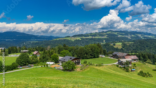 Panorama of the Lower Bregenzerwald featuring the villages of Alberschwende, Langenegg, and Sulzberg. Meadows, farmhouses, and forests in Austria; blue sky with storm clouds in the background.