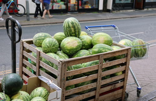 Large crate of watermelons on sale on the side of a busy urban street