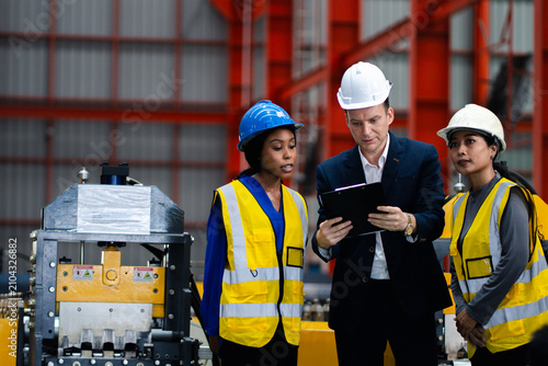 Industrial teamwork and digital manufacturing. Engineers review production data using a laptop and tablet beside factory machinery. Industry, teamwork, technology, inspection, production