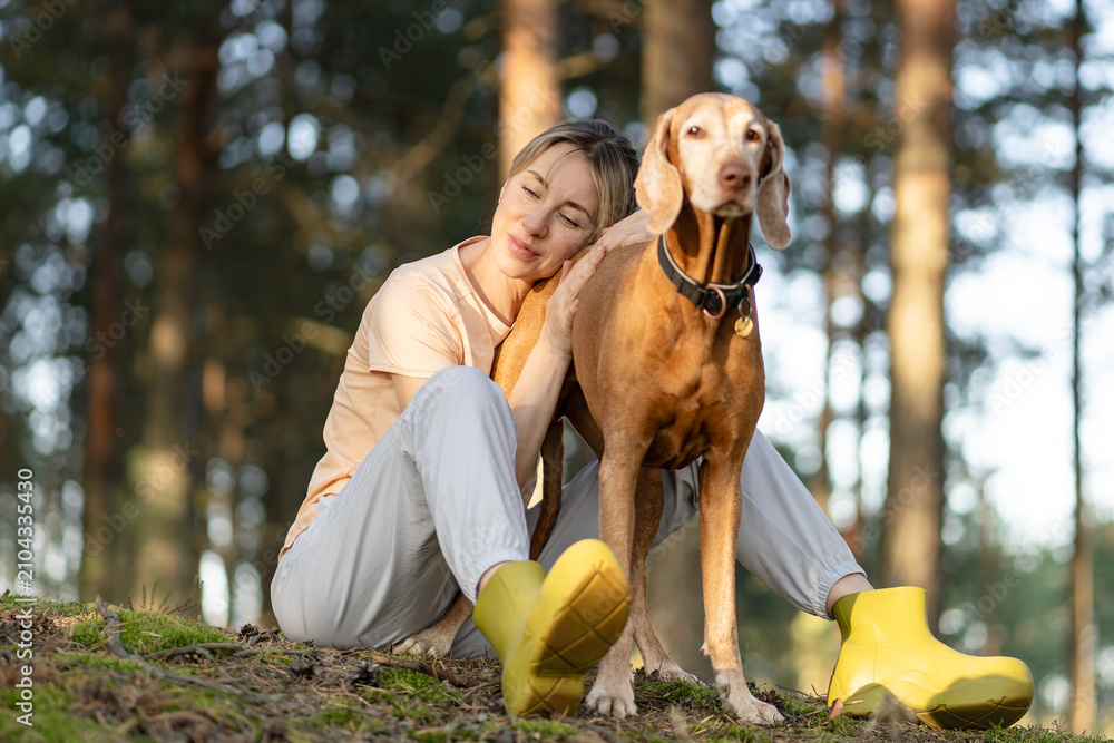 Obraz premium Recreation, building relationships and trust with pet, tranquil woman hiker relaxing in forest with dog, positive female sitting resting head on dogs back enjoying nature, daily walk for mental health