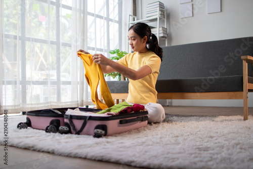 Woman packing clothes for a trip. Young woman packs clothes into a suitcase in room, getting ready for an upcoming trip.