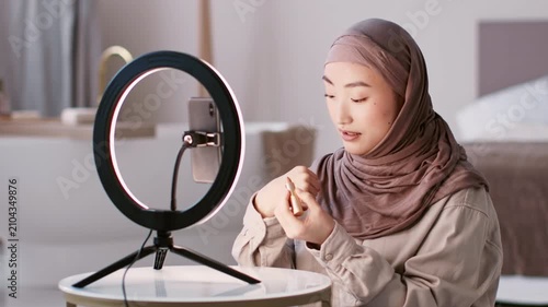 Focused Young Asian Woman Applying Makeup With Care In Front Of Ring Light At Home, Engaging In Skincare Routine. Creating Beautiful Look In Contemporary Indoor Setting. Beauty Concept.