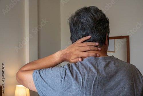 Middle-aged man with neck and occipital pain, standing indoors, medical healthcare and physiotherapy treatment concept.