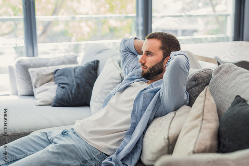 Fotografía Young man relaxing on a comfortable sofa in a bright living room, enjoying quiet