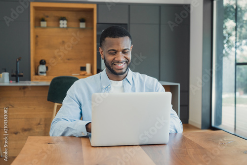 Foto African american man smiling while engaging with his laptop, enjoying remote wor