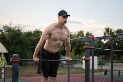 A man does pull-ups on bars at a park gym in the afternoon. He is focused and working out his muscles