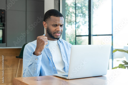 Photos Young black man experiencing computer issues, showing frustration and stress whi