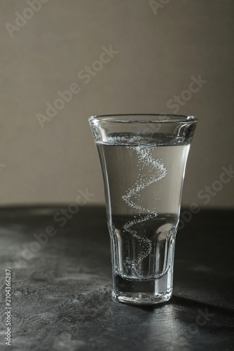A clear glass of sambuca on a dark surface with rising bubbles in a soft spiral.