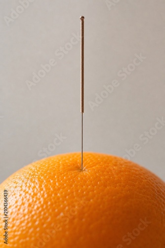 Acupuncture needle inserted into an orange peel in soft natural light.