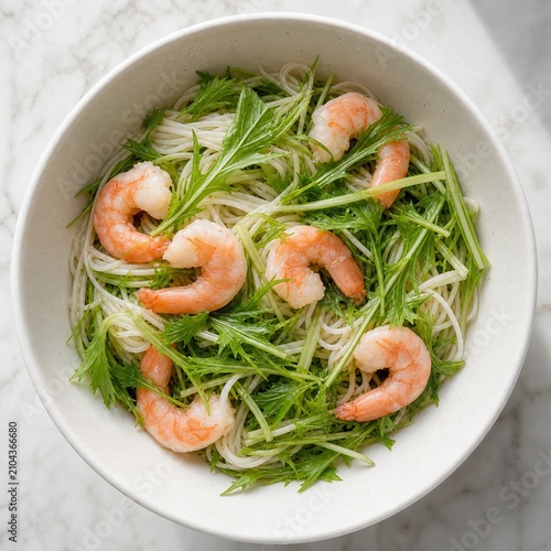 A white bowl with green mizuna, pink shrimp, and noodles, top-down view.