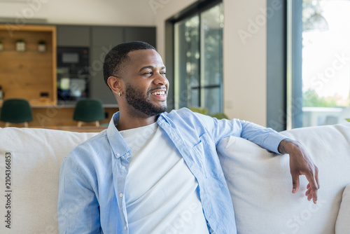 Canvastavla Smiling young man relaxes on a comfortable sofa in a bright, open-plan living room