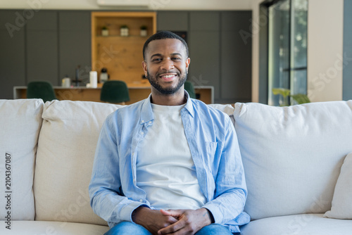 Foto Young handsome african american man is sitting comfortably on a modern couch in