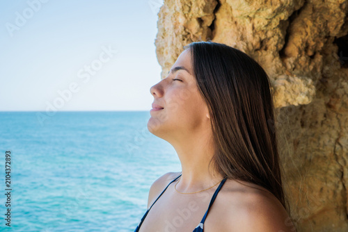 Konstfotografi Young woman standing by a rocky cliff overlooking the ocean with eyes closed, fi