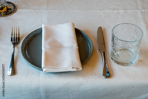 Modern table setting with ceramic plate folded white napkin knife fork and drinking glass viewed from above