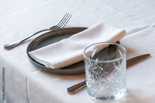 Elegant restaurant table setting with white cloth napkin ceramic plate drinking glass and polished cutlery