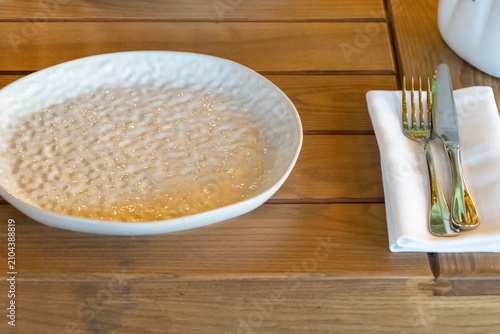 Empty ceramic restaurant plate on wooden table with folded napkin and cutlery prepared for elegant dining service