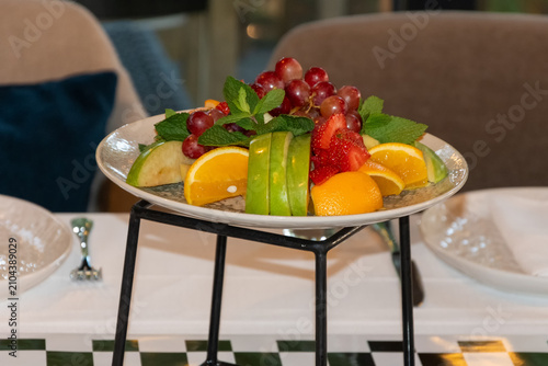 Fresh assorted fruit platter with grapes apples oranges strawberries and mint served in elegant restaurant interior